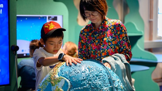 Child and mother exploring a globe in Curiosum's exhibition about earth.