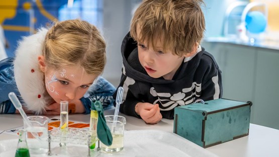 Två barn gör häxan Agata Densitatas spannande kemiexperiment på Curiosum