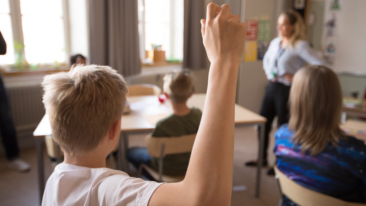 Mellanstadiebarn i klassrum. Pojke räcker upp handen.