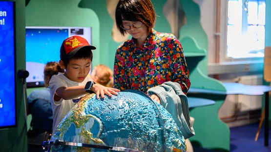 Barn och mamma utforskar jordglob i Curiosums utställning Jorden